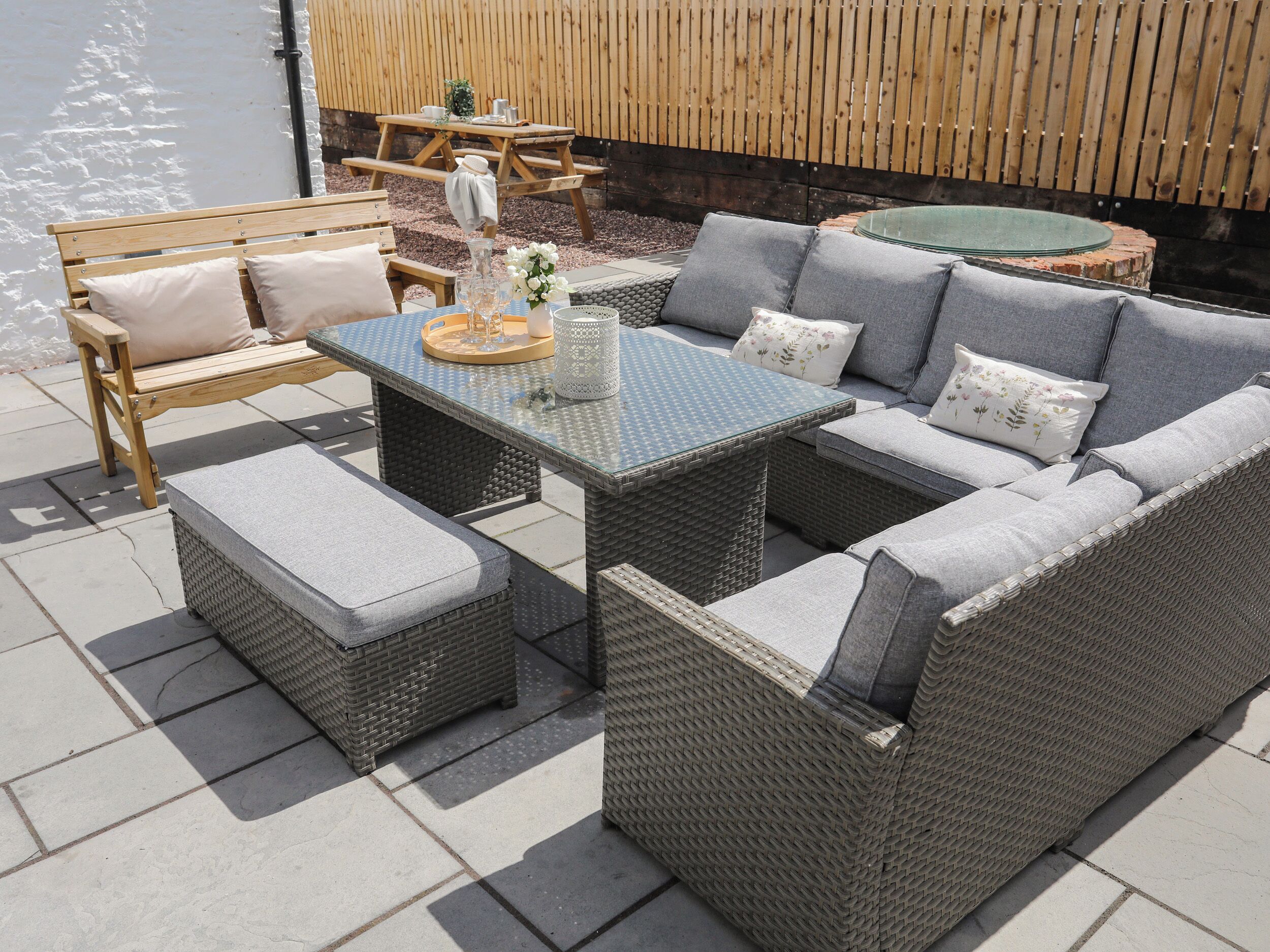 Eine Terrasse mit Korbmöbeln, darunter ein Sofa, ein Hocker und ein Tisch mit Glasplatte.