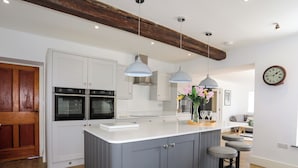 A modern kitchen with white cabinets, two ovens, a central island, pendant lights, and a wooden floor. - Plas Coch (Saint Asaph)