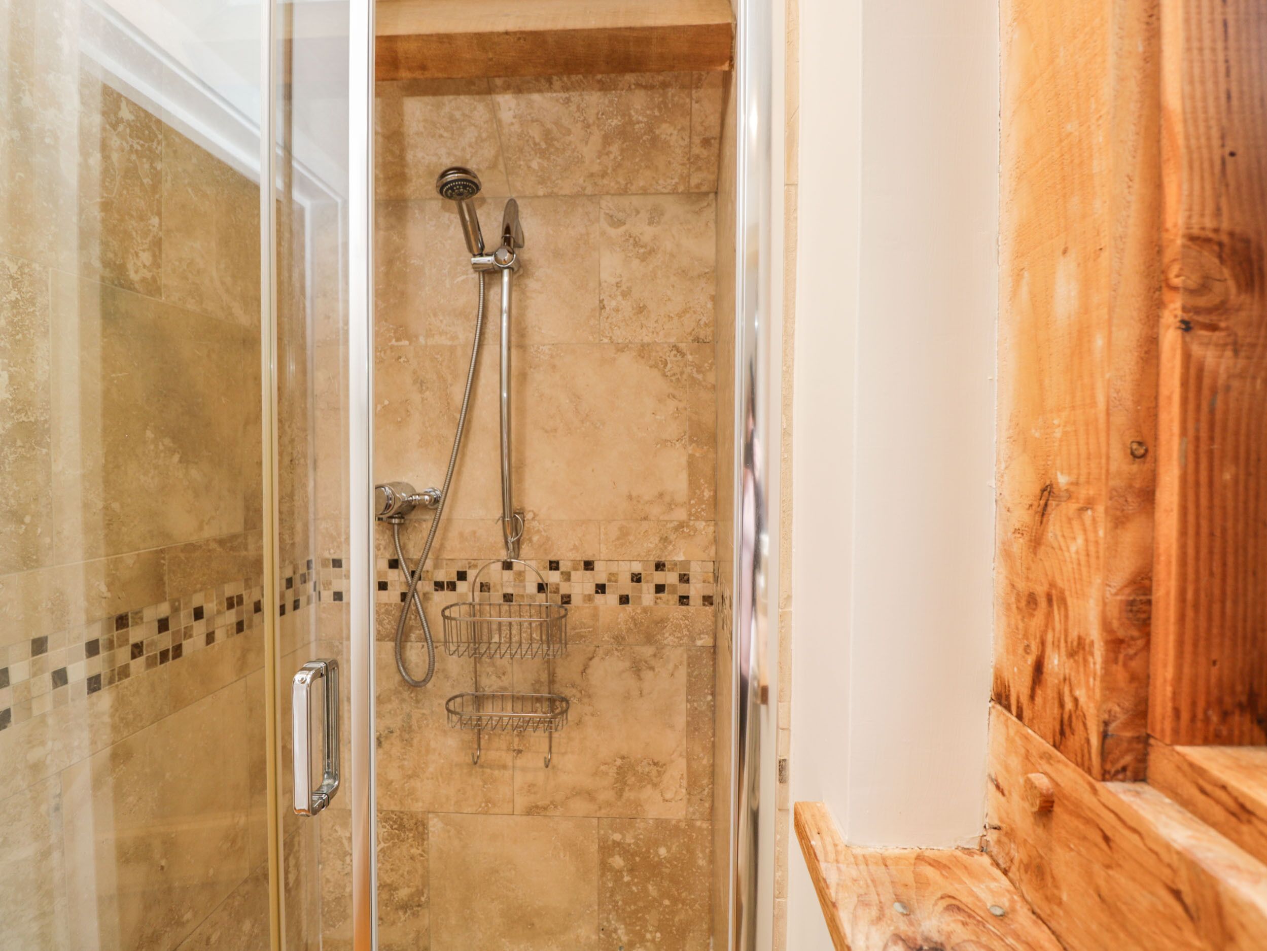 A glass-enclosed shower area with a wooden bench and a tiled wall.