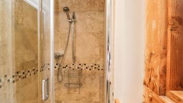 A glass-enclosed shower area with a wooden bench and a tiled wall.