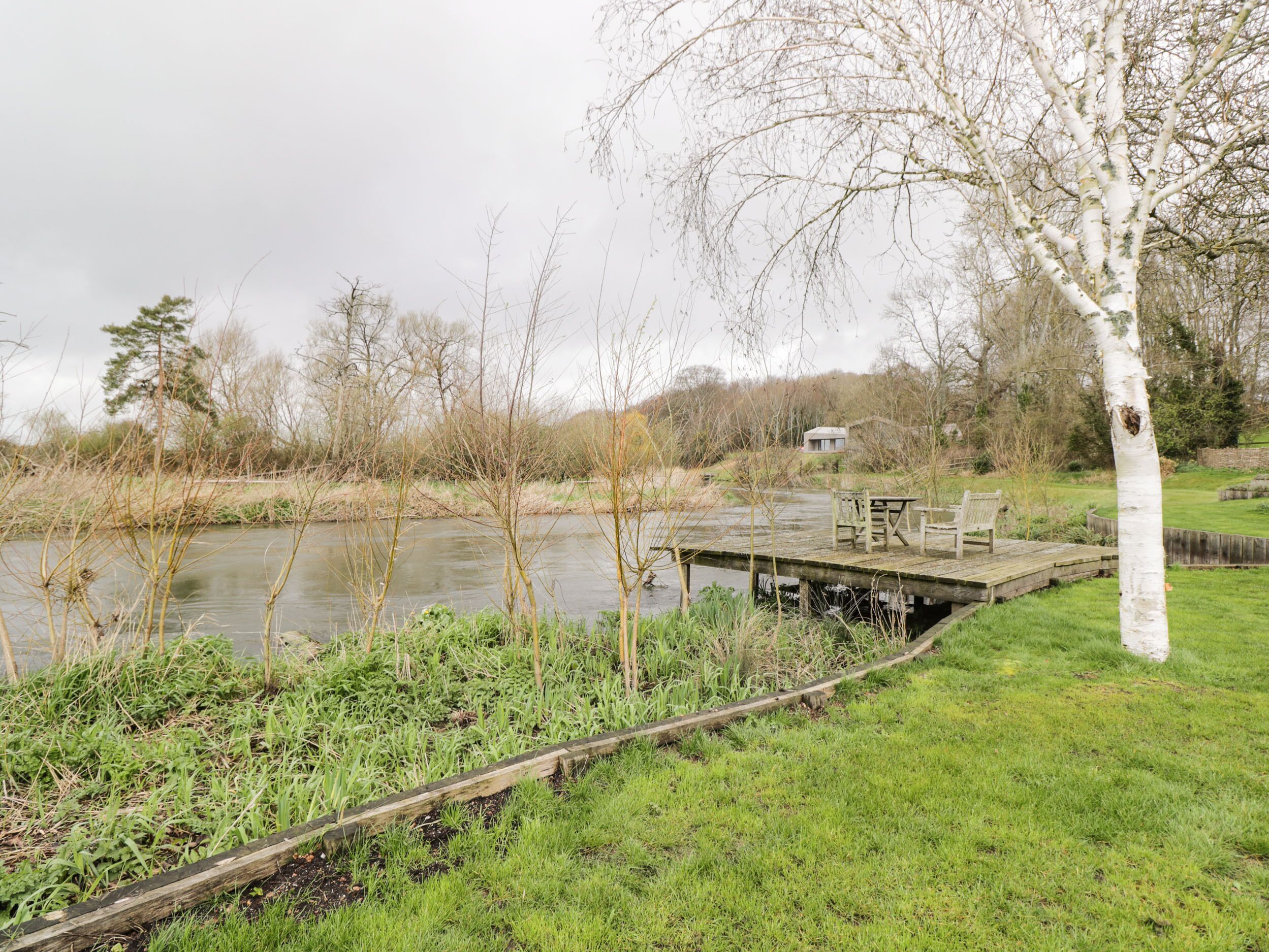 A riverside park with a wooden deck, benches, and a small building in the background.