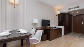 Quarto de hotel moderno com área de refeições, televisão de tela plana e cozinha compacta.