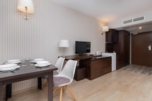 A modern hotel room with a dining area, a flat-screen TV, and a kitchenette.