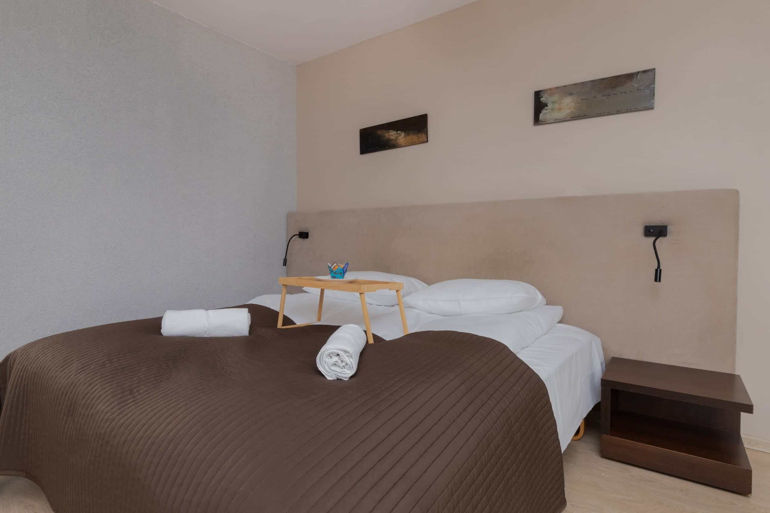 Ein modernes Hotelzimmer mit einem großen Bett, einem Holfnachtkästchen, einem kleinen Tisch und zwei an der Wand befestigten Kunstwerken.