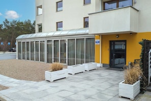 Un edificio moderno con facciata gialla, ingresso coperto e cartello che indica un’area di parcheggio 7C.
