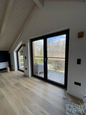 A spacious room with a large sliding glass door leading to an outdoor deck, a wooden floor, and a white wall with a small wooden shelf. - Vacation home with large sun terrace (Edertal)