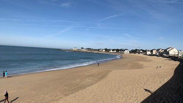 Una extensa playa de arena con cielo azul despejado y mar en calma.