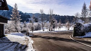 A snow-covered road with a wooden building on the left and a mountain in the background. - Großzügige Wohnung für bis zu 5 Persone in Steibis (Oberstaufen)