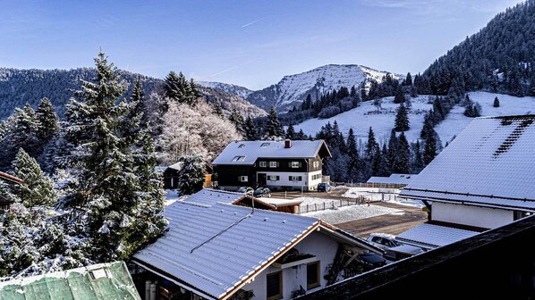 A snow-covered mountain village with a two-story house featuring a sloped roof and a visible garage.