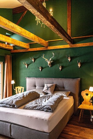 Ein Schlafzimmer mit einem großen Bett, Holzbalken, einer grünen Wand und an der Wand befestigten Tierkopfpräparaten.
