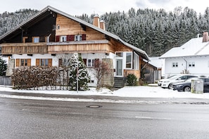 A wooden chalet with a balcony, a stone facade, and a snow-covered landscape.