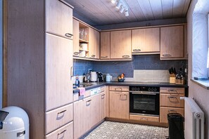 Eine kleine Küche mit Holzausstattung, einem Siemens-Ofen und einer gefliesten Spritzschutzwand.