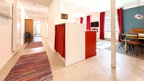 Ein modernes Hotelzimmer mit Küchenzeile, einem Essbereich und einem großen Fenster mit roten Vorhängen.