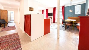 Ein modernes Apartment mit Küche, Essbereich und Wohnzimmer. Es zeichnet sich durch eine Farbgestaltung in Rot und Weiß aus, verfügt über einen Flachbildfernseher und ein großes Fenster mit roten Vorhängen.