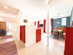 Un apartamento moderno con cocina, comedor y sala de estar. Presenta una decoración en tonos rojo y blanco, un televisor de pantalla plana y un amplio ventanal con cortinas rojas.
