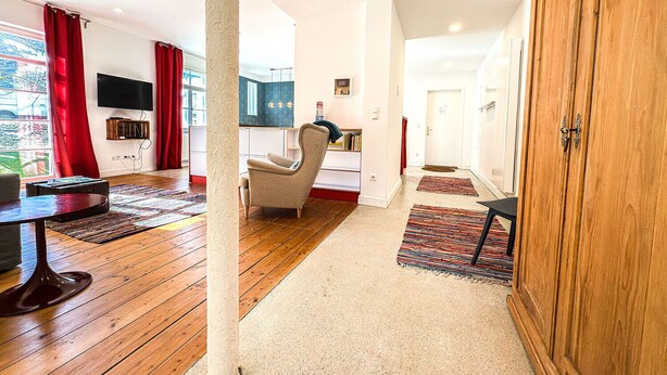Ein modernes Wohnzimmer mit Holzboden, einem beige gefärbten Sessel, einem an der Wand befestigten Fernseher und einem Holzschrank.