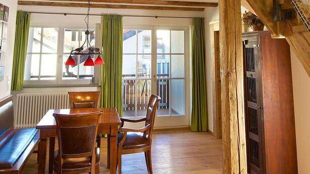 Amplia habitación con una escalera de madera, zona de comedor con mesa y sillas, y vistas a través de grandes ventanales.