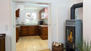 Una cocina moderna con armarios de madera, estufa de piedra y vistas a un comedor por medio de una puerta de vidrio.