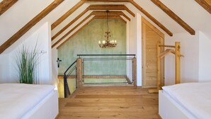 Una escalera estrecha con vigas de madera y una pared verde, que lleva a una habitación con cama y una lámpara colgante.