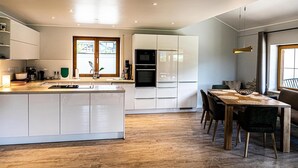 Eine moderne Küche mit weißen Schränken, einer zentralen Kochinsel und einem Essbereich mit Holztisch und Stühlen.