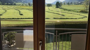Blick aus einem Fenster mit Metallgitter auf terrassierte Felder und ferne Hügel.