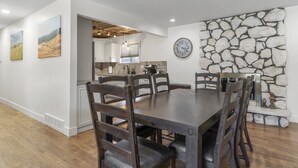A dining area with a stone wall, a clock, and a view into the kitchen.