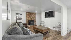 A modern living room with a brick fireplace, a flat-screen TV mounted on the wall, and a grey sofa with patterned cushions.