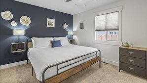A bedroom with a bed, bedside lamps, a ceiling fan, a window with blinds, and a dresser.