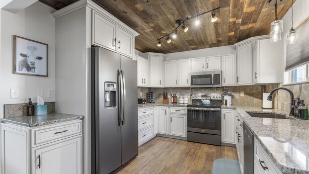 A modern kitchen with white cabinets, stainless steel appliances, and a wooden ceiling.
