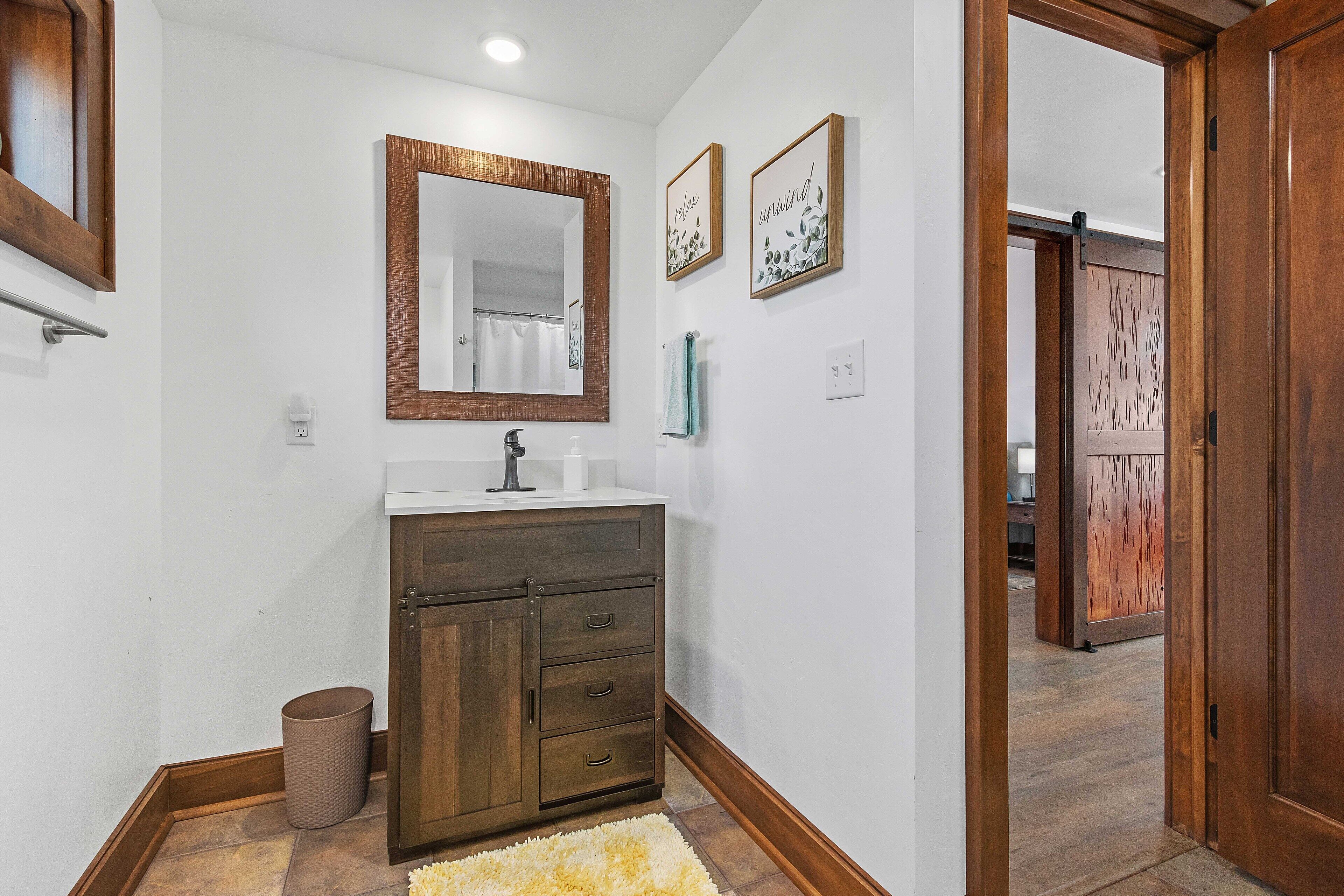 A bathroom with a wooden vanity, a mirror, and two framed signs on the wall.