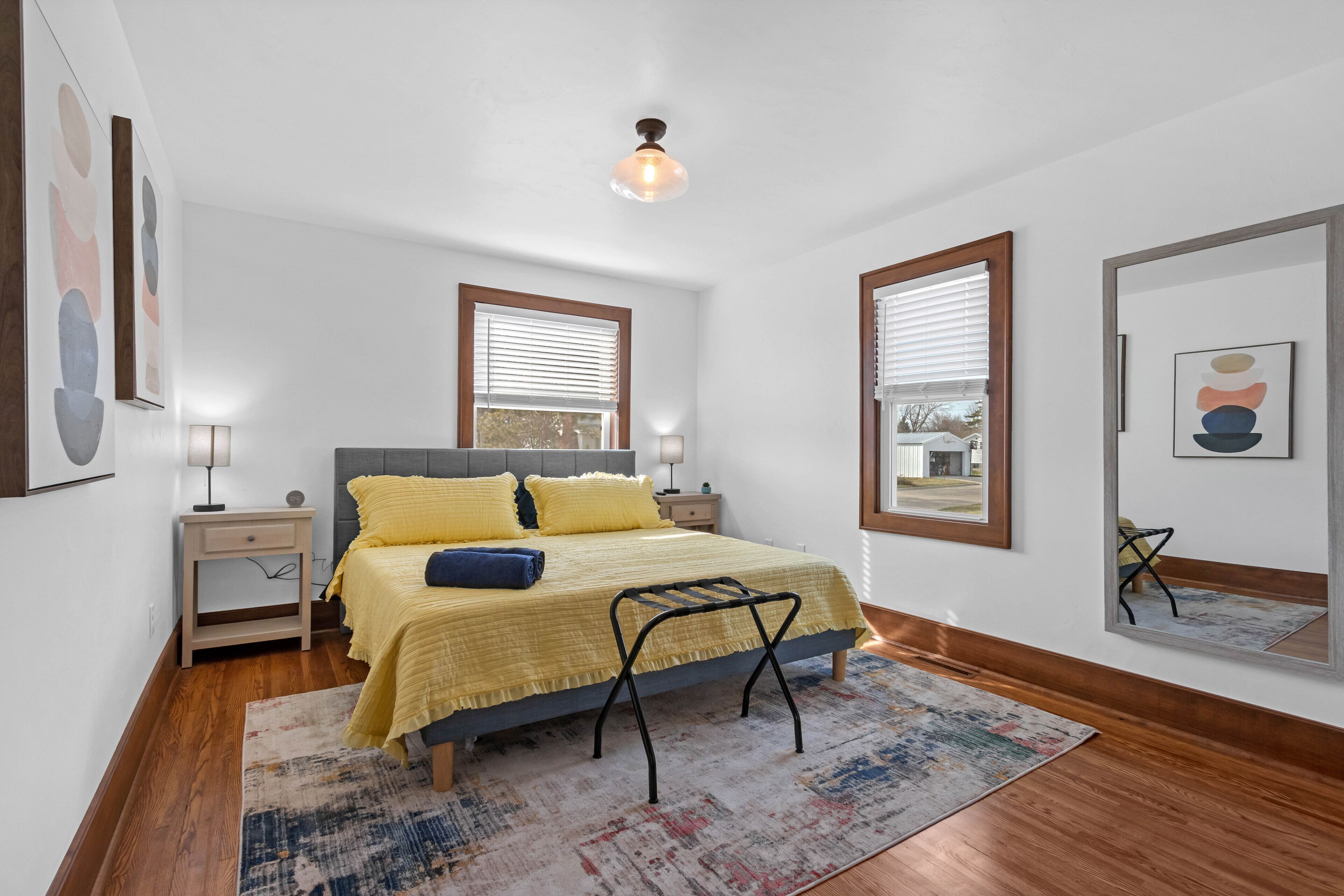 Une chambre à coucher comprenant un lit, des tables de chevet, une commode, un miroir et une fenêtre avec des stores.