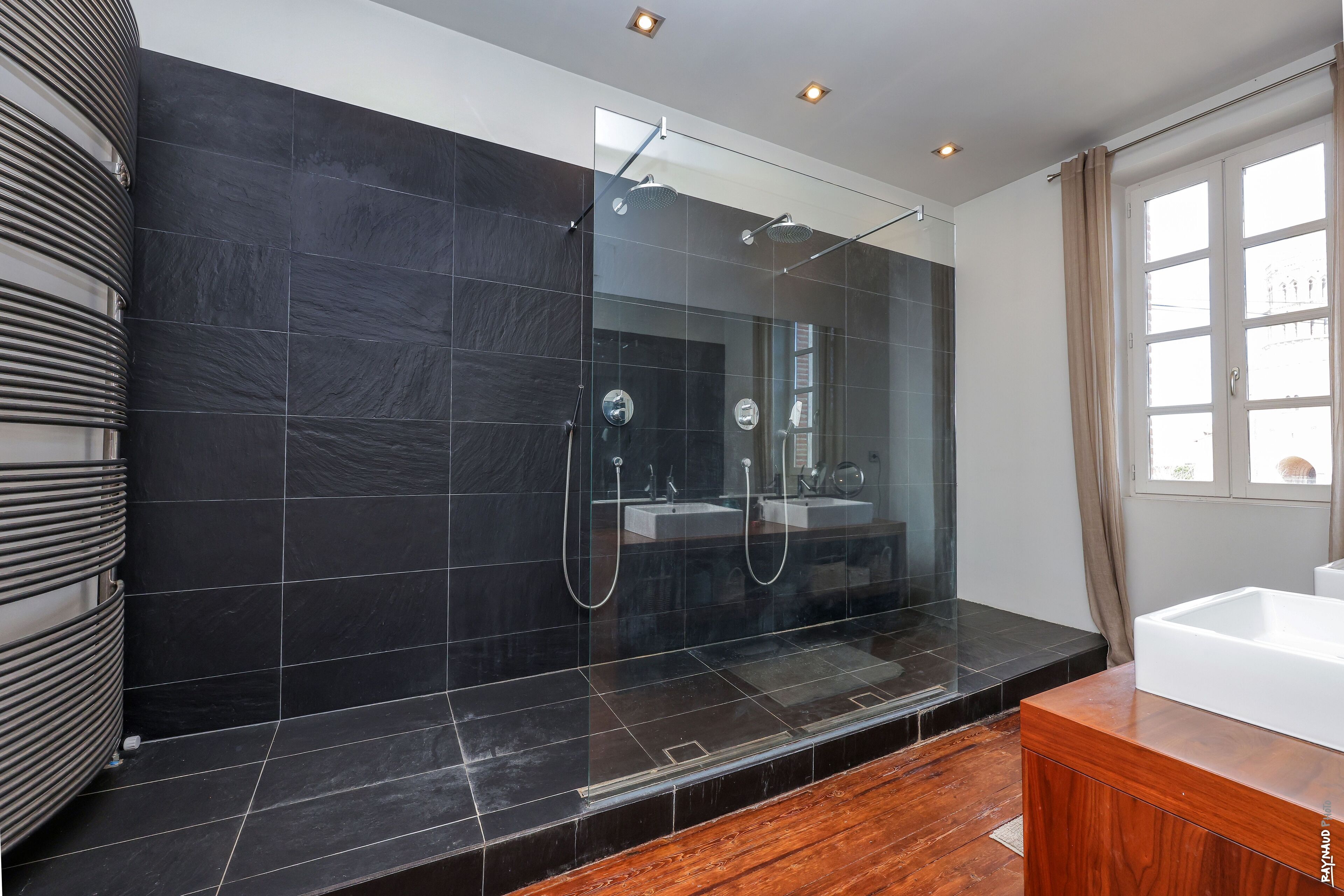 A modern bathroom with a glass-enclosed shower, a wooden vanity, and a large window.