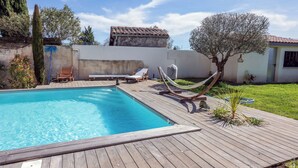 Ein Schwimmbecken mit Holzterrasse, Liegestühlen und einer Hängematte.