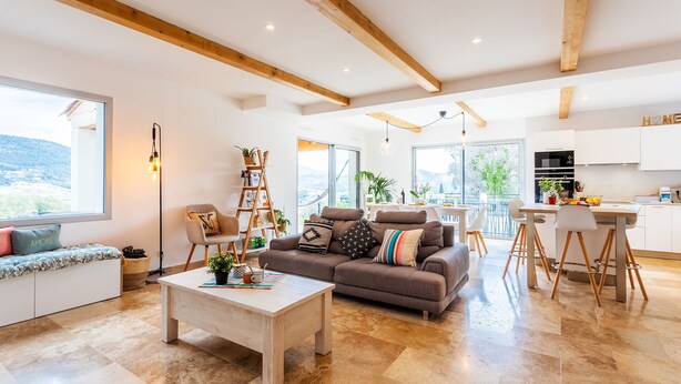 Ein geräumiges Wohnzimmer mit einer großen Couch, einem Couchtisch und einem Essbereich, im Hintergrund ist eine Küche zu sehen.
