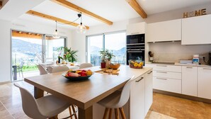 Eine moderne Küche mit weißen Schränken, einem Holzespeisetisch und Blick auf Berge durch große Fenster.