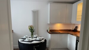 Una cucina compatta con mobili bianchi, un piano di lavoro in legno e un'area pranzo con un tavolo rotondo e sedie nere.