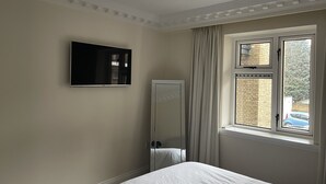 Una camera da letto con un letto, una TV a schermo piatto montata a parete, uno specchio a figura intera e una finestra con tende.