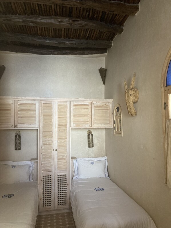 A bedroom with two beds, wooden headboards, a woven wall decoration, and a small window.