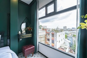 A room with a view of a cityscape through a large window, a bed, a vanity with a mirror, and a red bench. - Collection O VyVy Airport Hotel (Ho Chi Minh City)