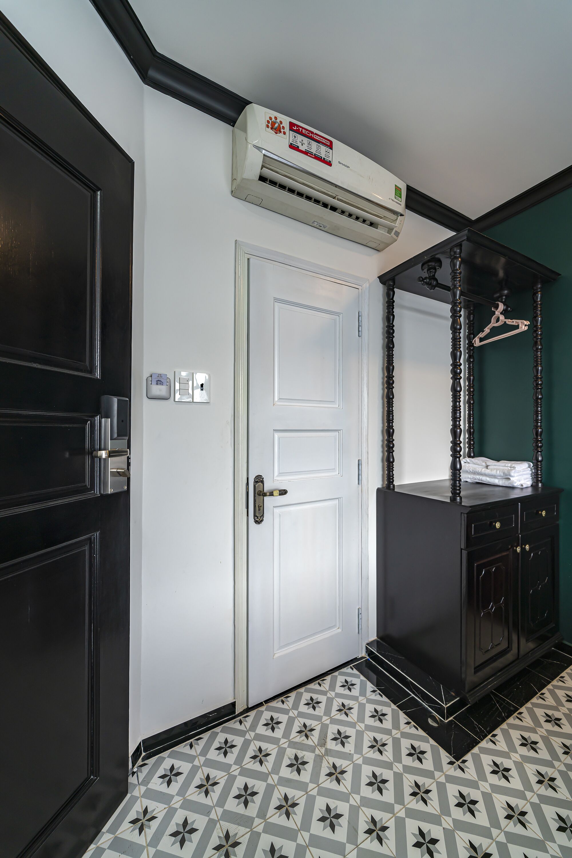 A hallway with a white door, a black wardrobe, and a patterned floor.