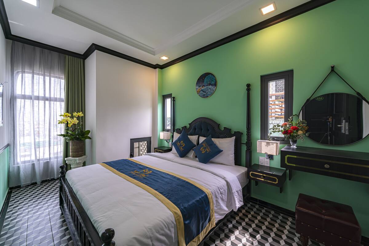 Une chambre d’hôtel avec un grand lit, une table de chevet, une commode et un mur vert.