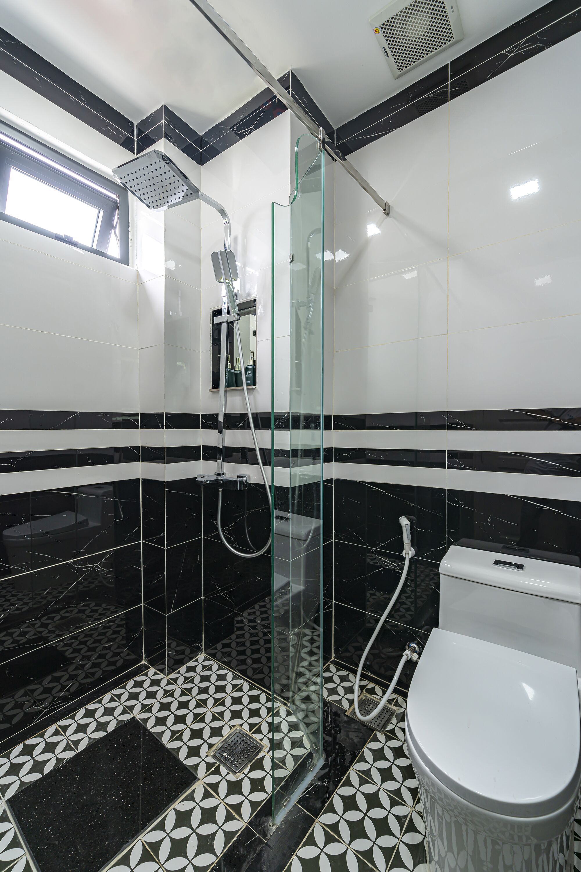 A modern bathroom with a glass-enclosed shower, a toilet, and a patterned floor.