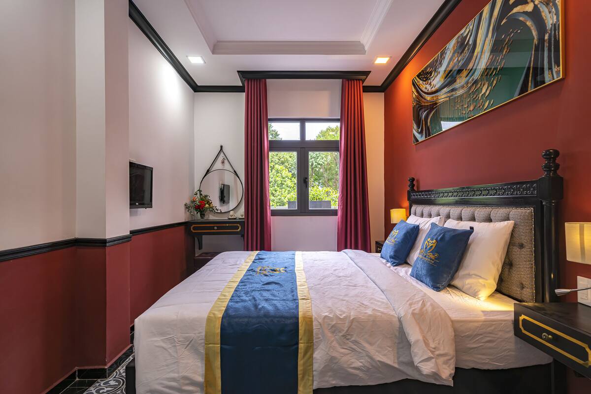 Une chambre d’hôtel avec un grand lit, une table de chevet, un miroir, une fenêtre avec des rideaux et un tableau au mur.