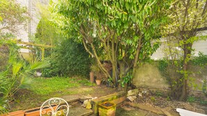 Un jardin avec un banc en bois, une chaise en métal et un bac à fleurs contenant des plantes.