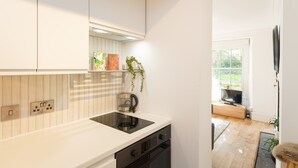Une cuisine moderne avec des meubles blancs, une cuisinière encastrée et une fenêtre qui laisse entrer la lumière naturelle.