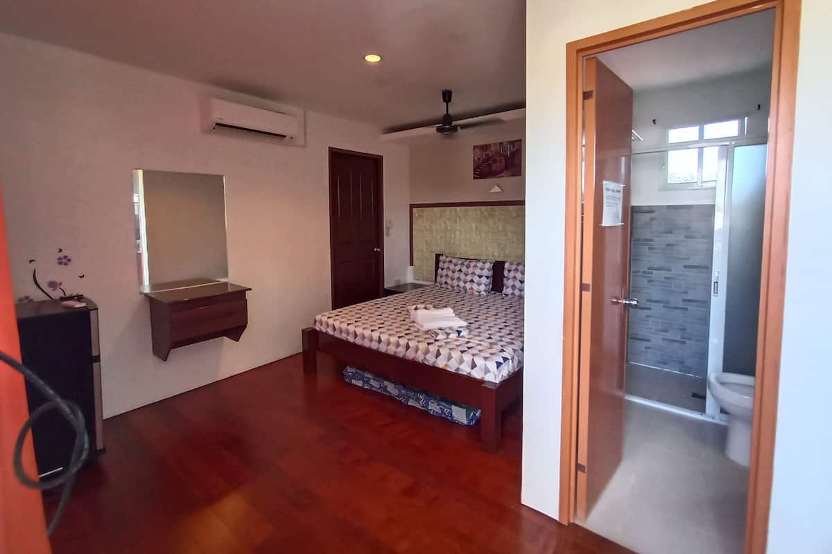 A bedroom with a bed, a desk, a mirror, a ceiling fan, and a bathroom visible through an open door.