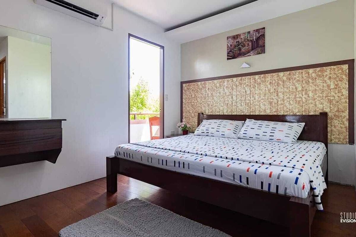 A bedroom with a bed, a dresser, a mirror, and a window.