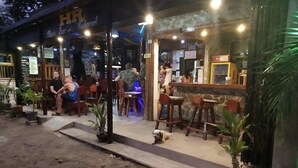 Uma área externa com mesas, cadeiras, um pequeno cão e plantas em vasos.