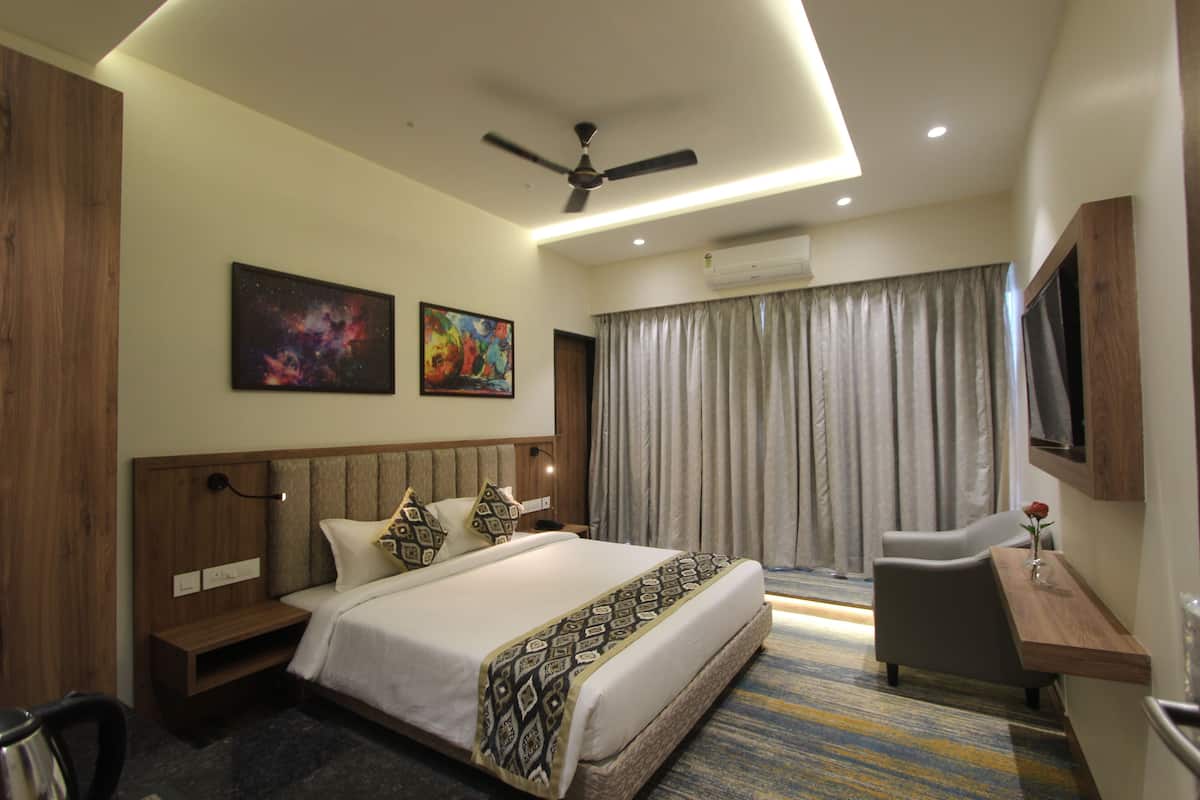 A modern hotel room with a large bed, a desk, a chair, a ceiling fan, and artwork on the walls.