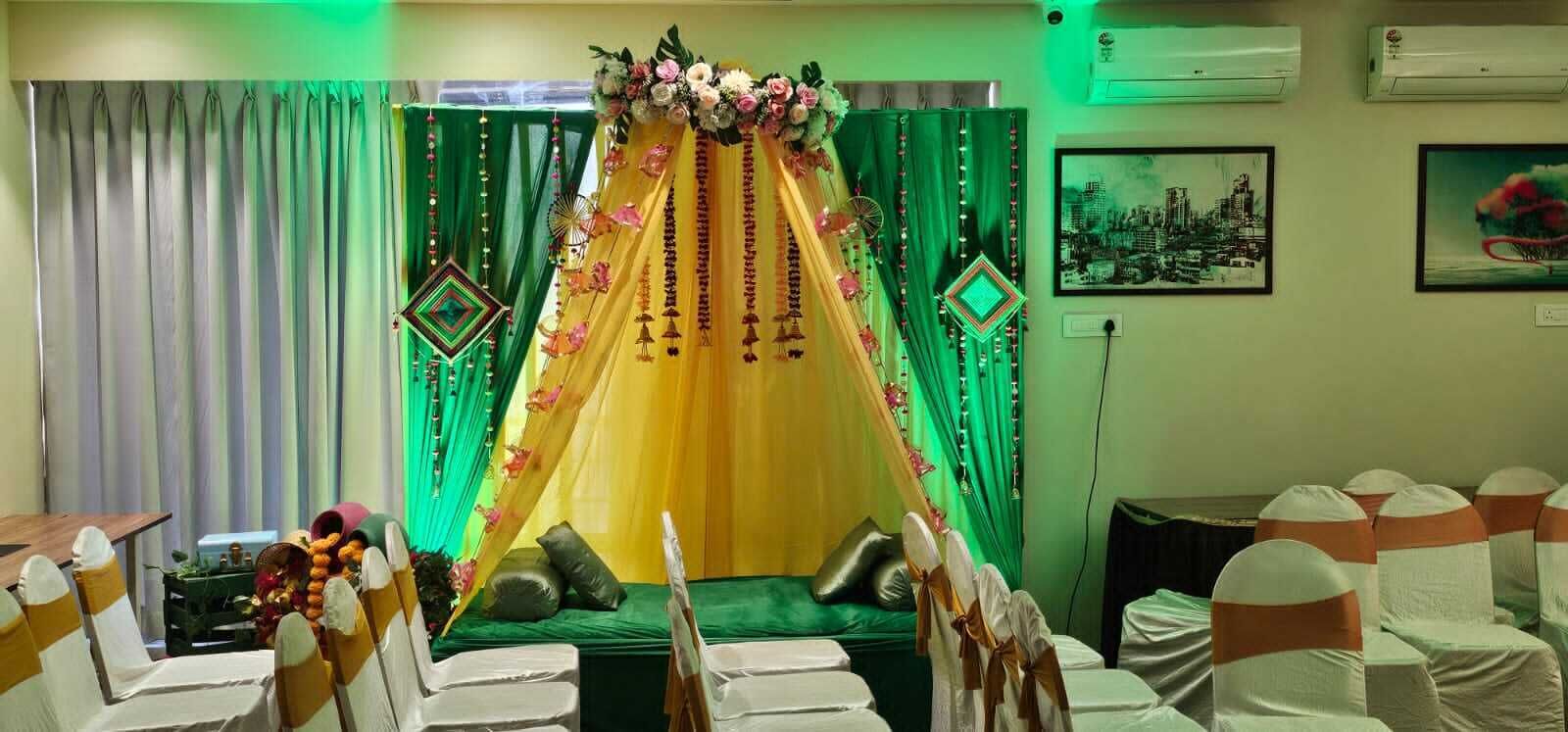 A room with a green and yellow canopy, white chairs with orange sashes, and a green curtain backdrop.